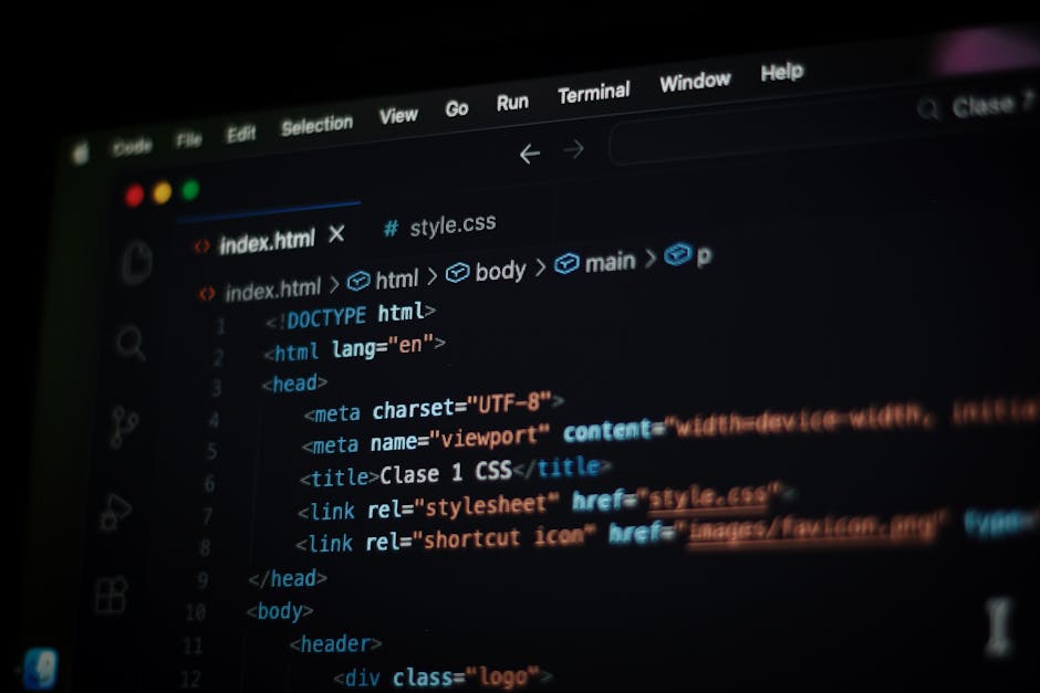 A close-up view of a person's hand operating a black computer keyboard on a desk in an office environment. The monitor in front displays lines of code or text in a programming interface, with a predom